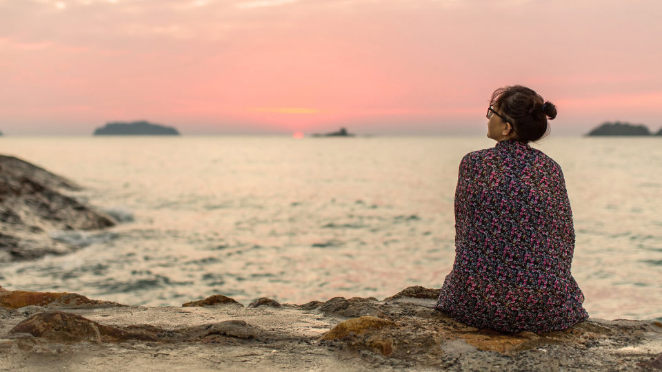 Woman sitting on the seashore watching the setting sun