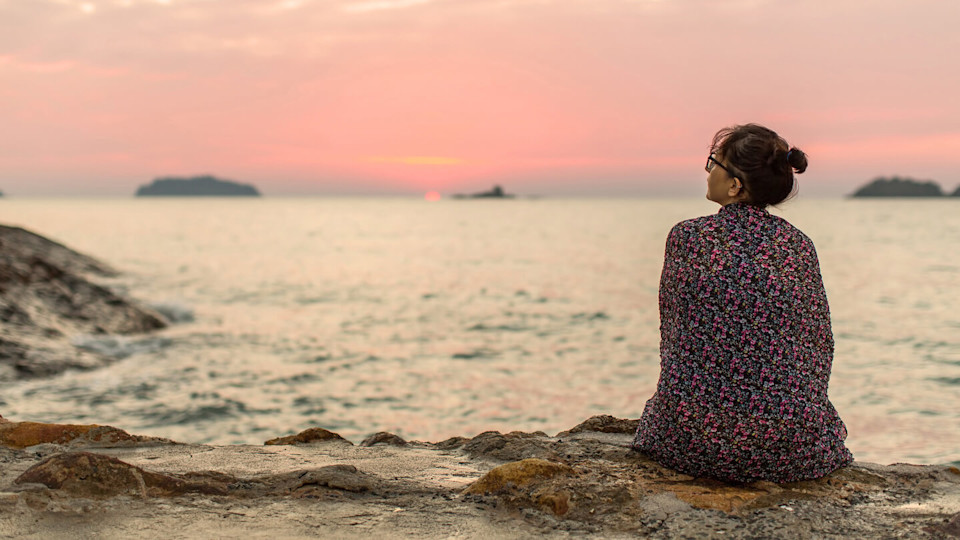 Woman sitting on the seashore watching the setting sun