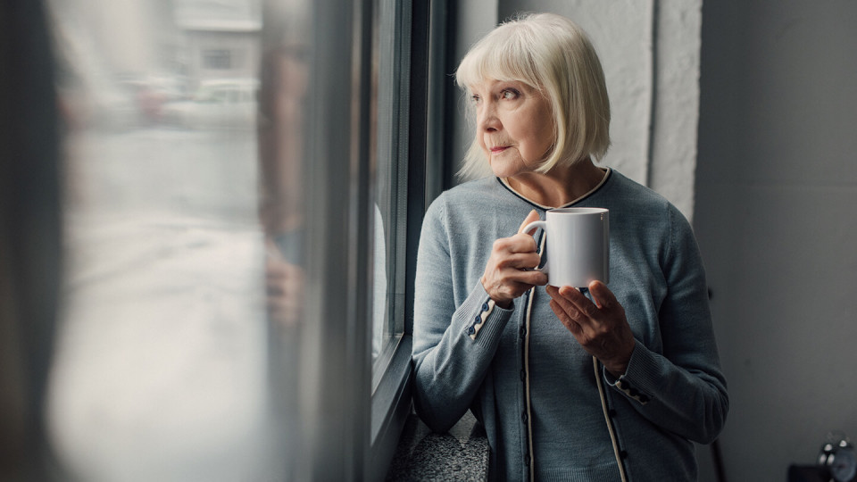 Mature woman with mug of coffee looking out of window