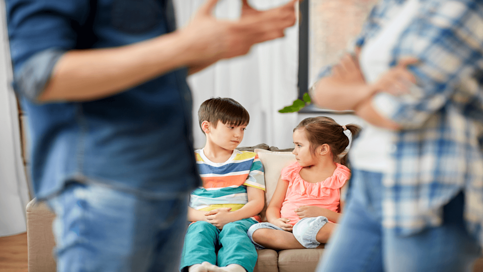 2 children on sofa in background with parents arguing in foreground - divorce