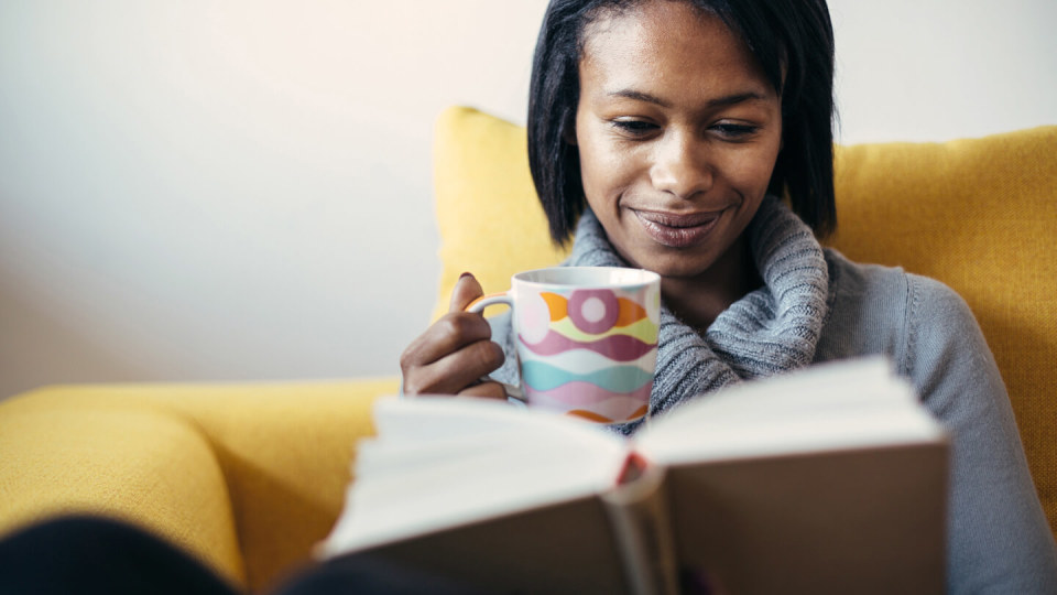 Woman drinking tea and reading book in cosy chair