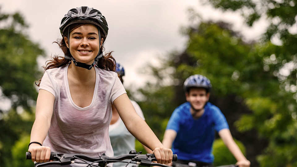 Female cyclist in white t-shirt and male cyclist in background.