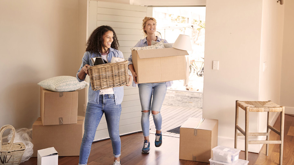Two women carrying boxes into a home