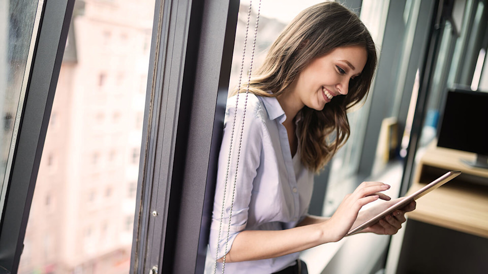 Happy woman sat by a window using an Ipad