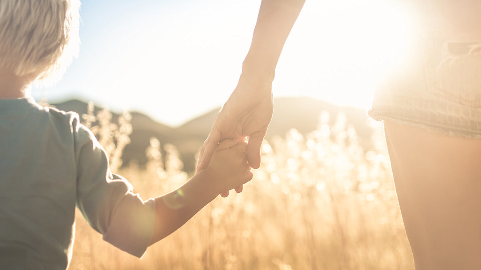 Parent holding hands with small child in sunny field