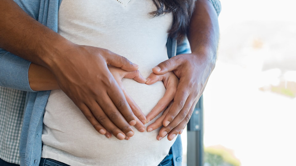 Parents cradling pregnancy bump, heart shape
