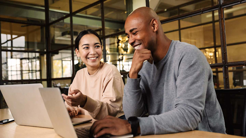 Two people working on laptops laughing