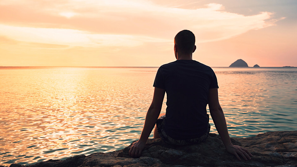 man sitting on the beach staring into the distance at sunset