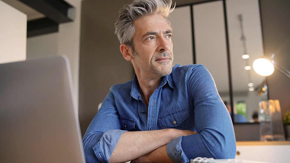 Man at laptop with arms crossed looking out window